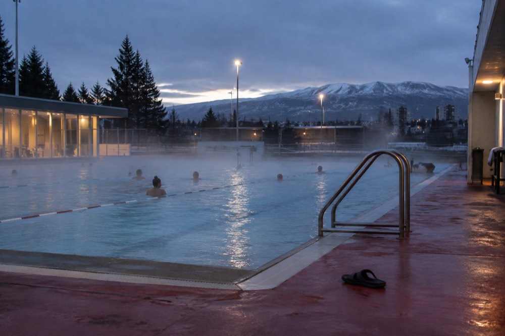 Steam drifting off a warm outdoor pool at dusk with city lights beyond
