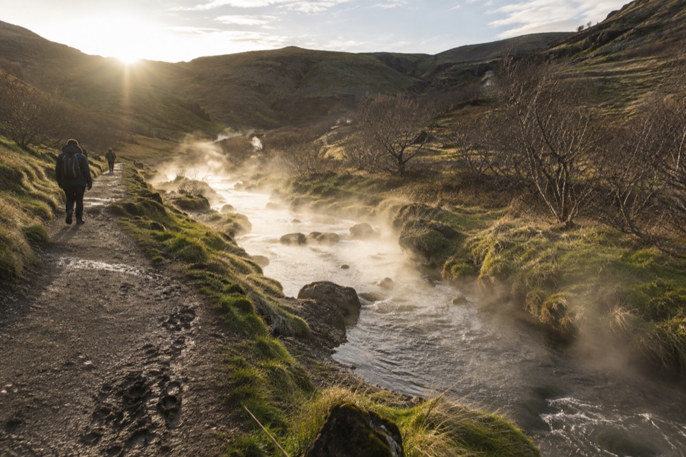 A steaming river winding through a green valley with a gravel path alongside