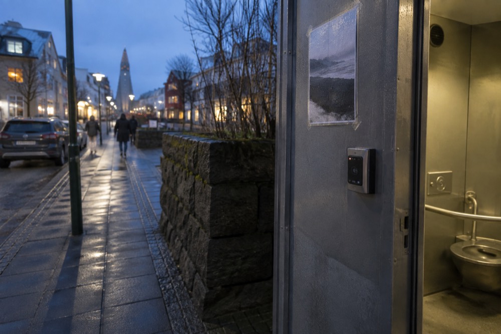 A card reader mounted on the door frame of a pay toilet stall in a Reykjavik tourist area