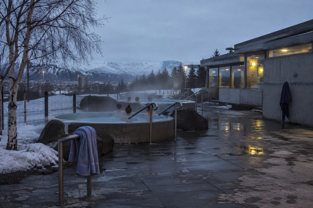 An Iceland swimming pool building with steam rising from outdoor hot pots in the evening