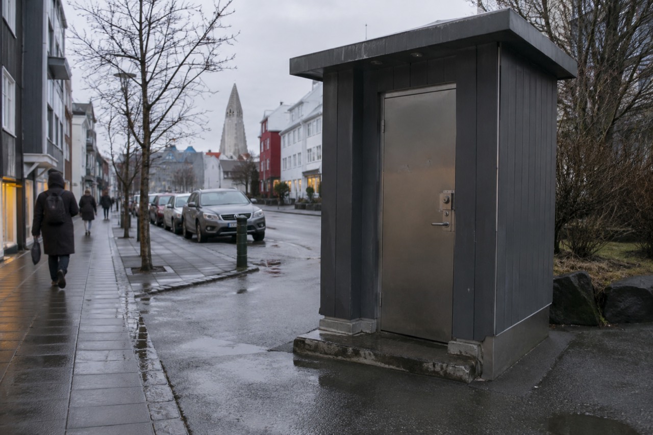 A clean single-stall public restroom with a coin-operated door latch on a Reykjavik side street
