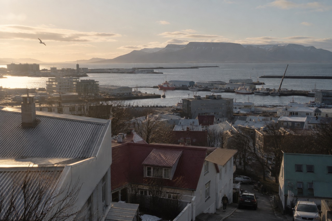 Reykjavik rooftops and harbour under a bright sky with mountains in the distance