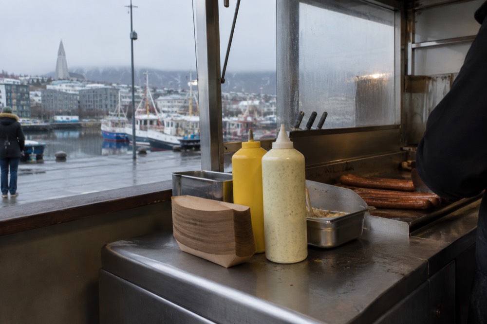 A hot dog stand counter with condiments and paper trays