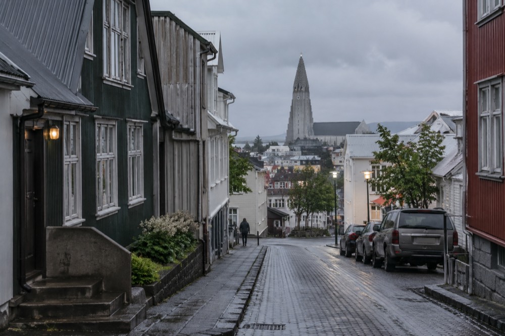 Church tower rising over downtown Reykjavik rooftops seen from a city street