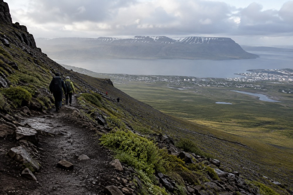 Mount Esja rises above a green valley with a trail winding upward through rocky slopes.