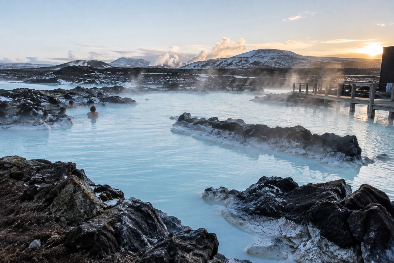 A wide view of the Blue Lagoon’s milky-blue water surrounded by black lava rock, steam rising in the cold air, with no people in sight.