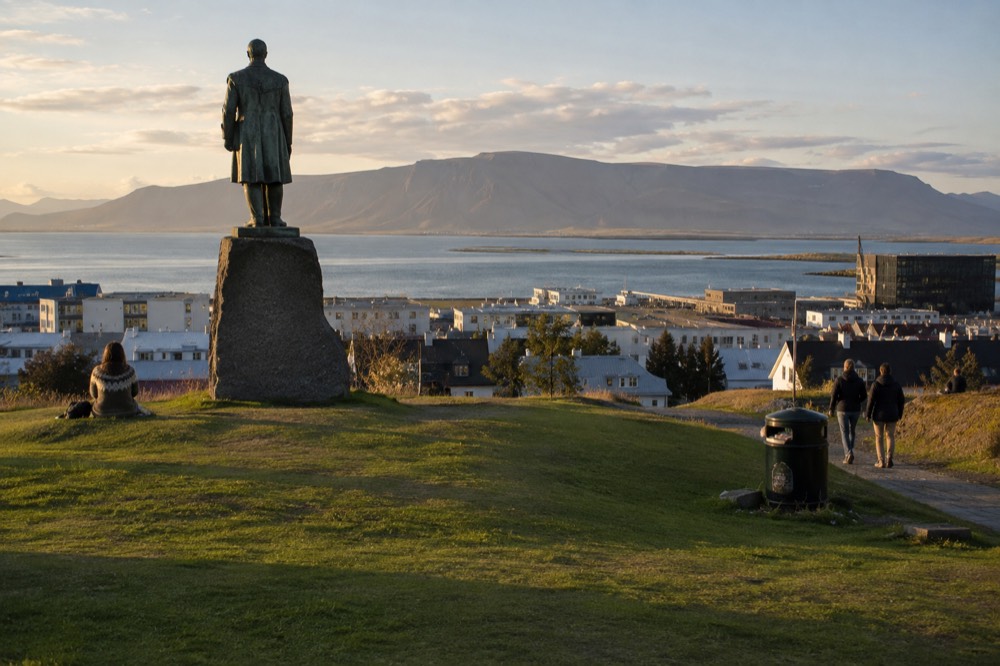 A hilltop statue overlooking a low city skyline with mountains in the distance