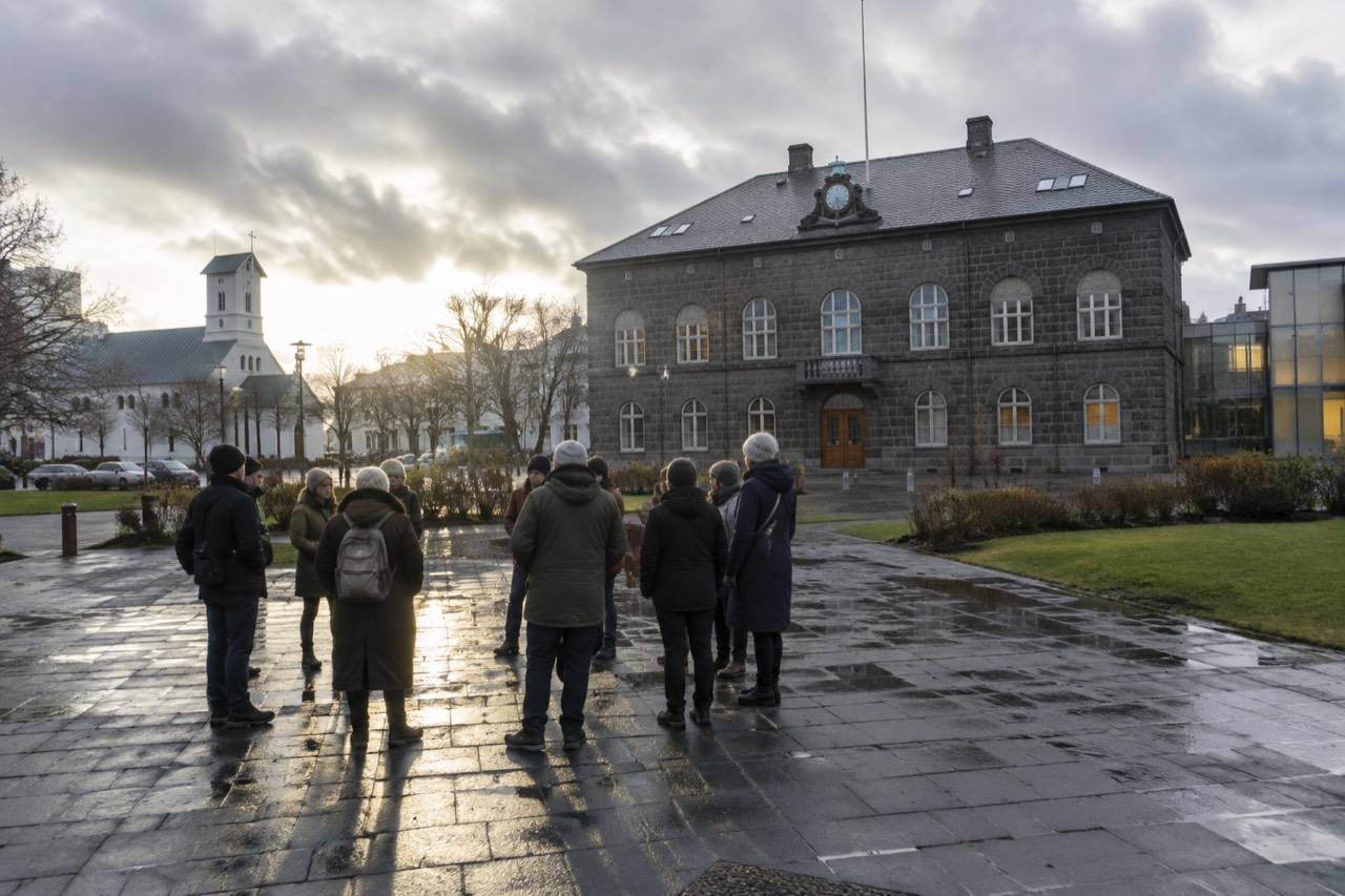 A guide with a small group of walkers standing on a cobbled square beside a stone parliament building in Reykjavik