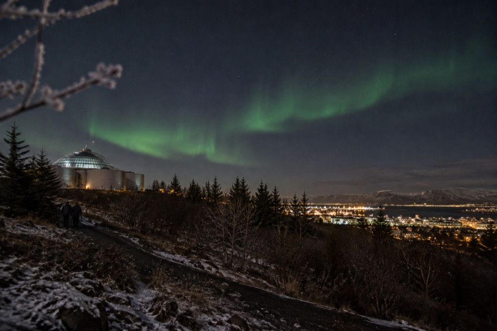 Green aurora glow above dark hillside on edge of Reykjavik