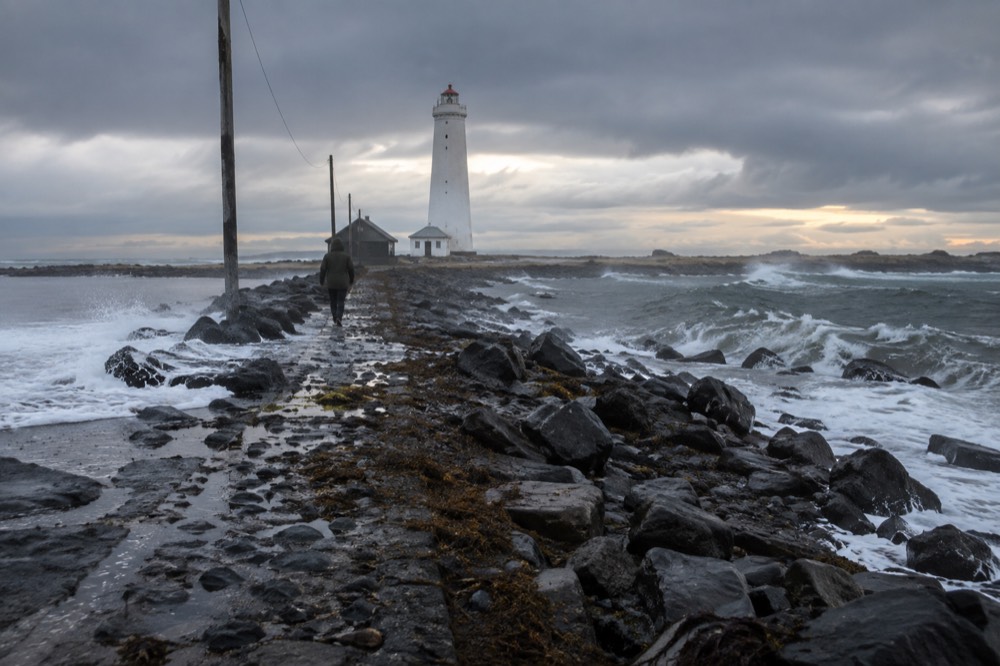 A lighthouse on a rocky causeway with waves on either side at low tide
