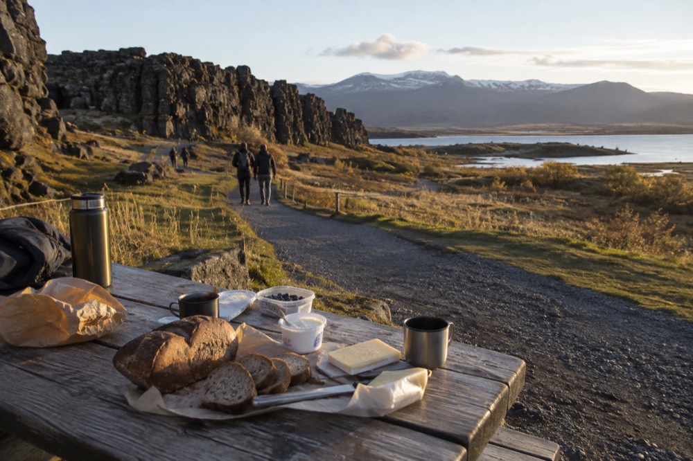 A picnic spread of bread, cheese and skyr on a bench beside a walking trail
