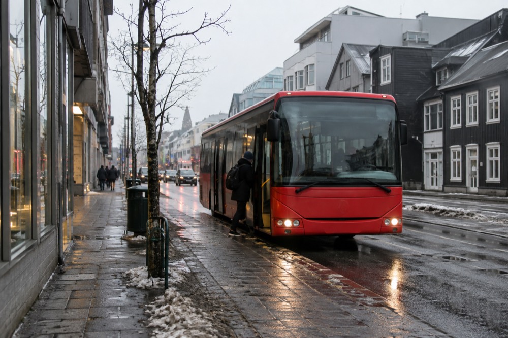 A red Reykjavik city bus at a stop on a quiet street