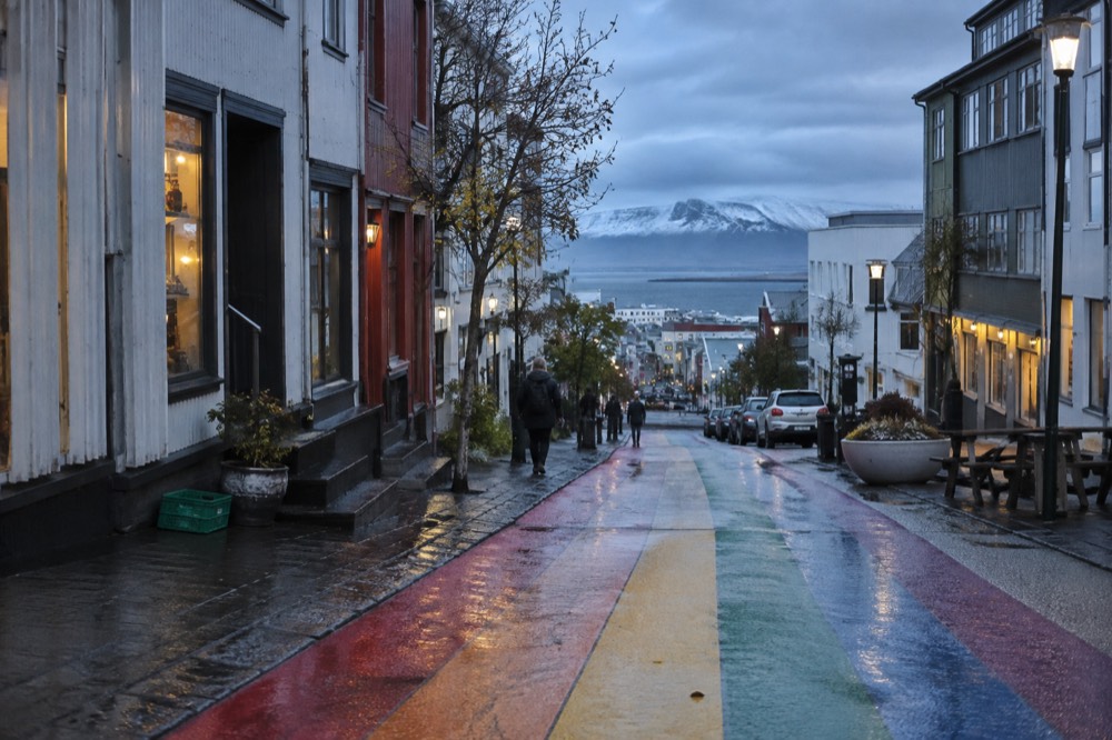 A rainbow painted street sloping down toward a harbour with small shops along both sides