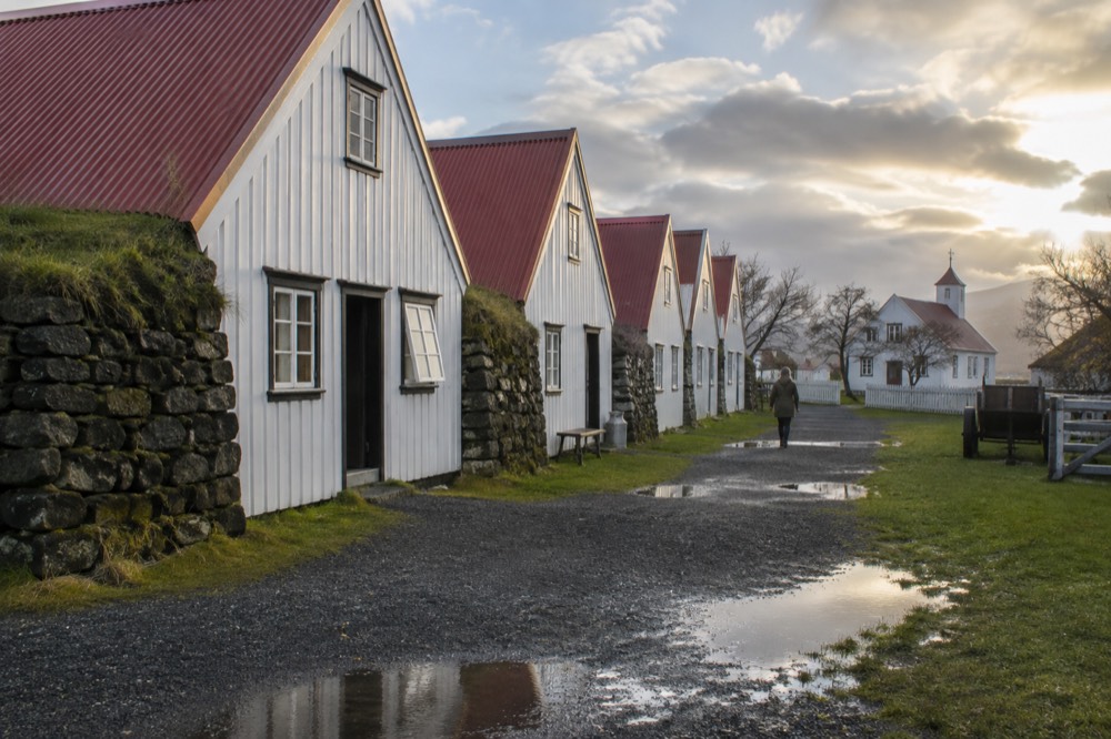 Row of restored historic timber houses with white walls and red roofs on a gravel path