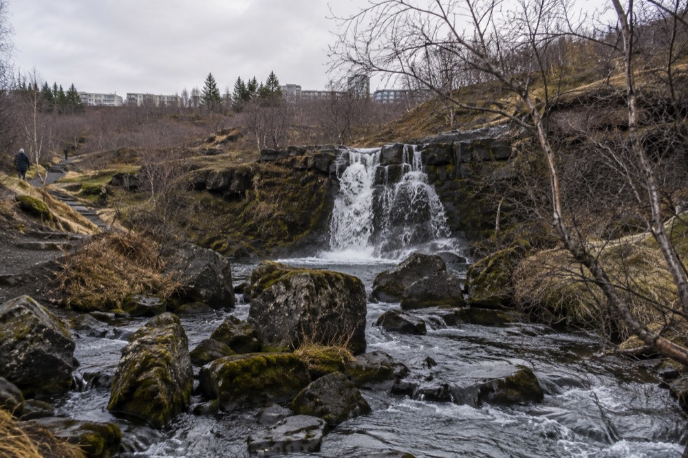 A small waterfall dropping over dark rocks in a wooded river valley