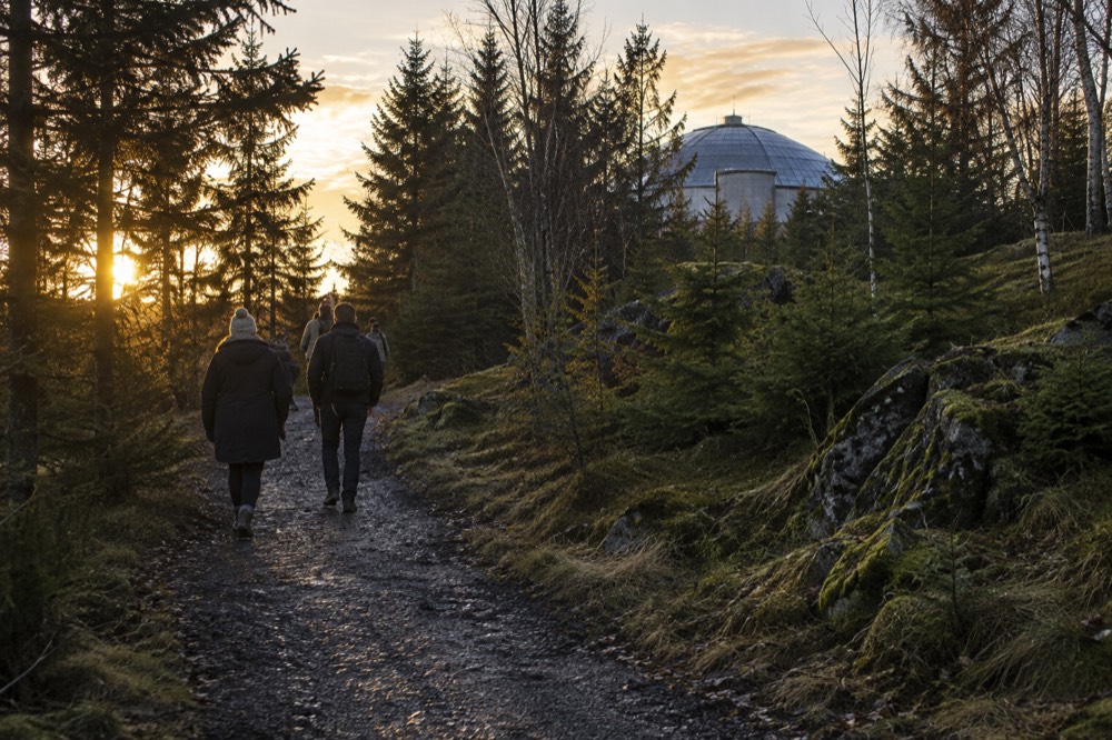 A woodland trail climbing a hill with a domed building visible above the treeline