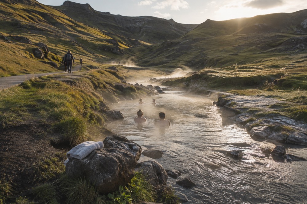 A steaming river running through a green valley with a footpath alongside it