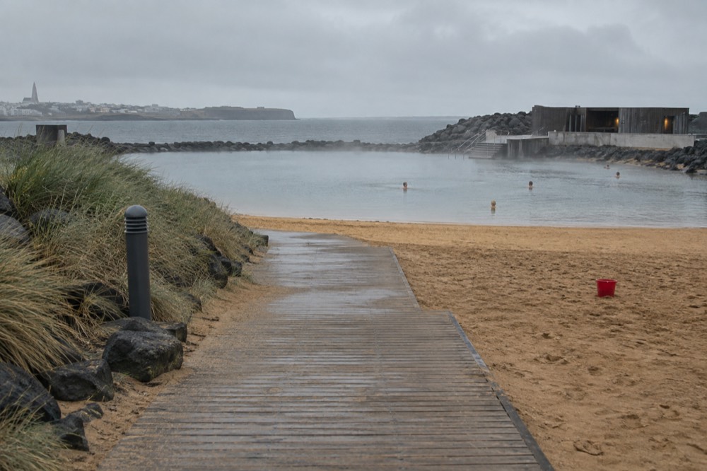 A geothermal lagoon area with a wooden boardwalk and a small sandy cove