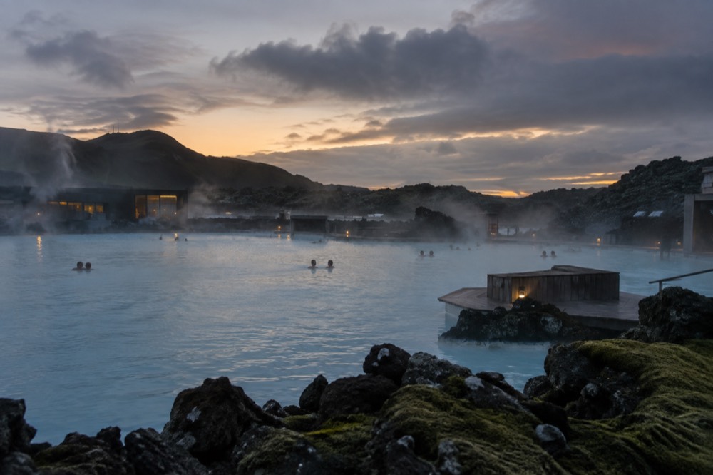Steam rising over a large man-made geothermal lagoon at dusk