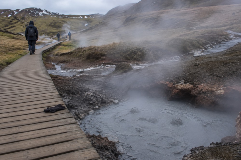 A wooden walkway passing steaming vents along a marked geothermal trail