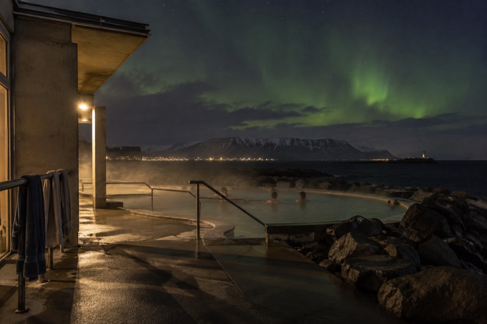 A steaming outdoor pool at night with faint green aurora above dark hills