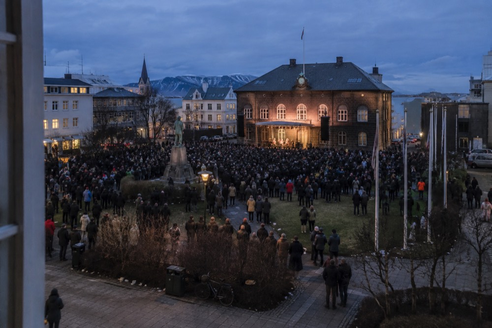 Crowd gathered in a city square at dusk with stage lights