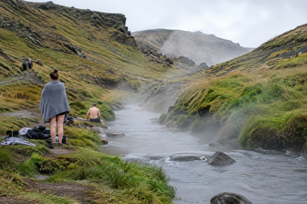 A steaming river running through a green valley with hikers on the bank