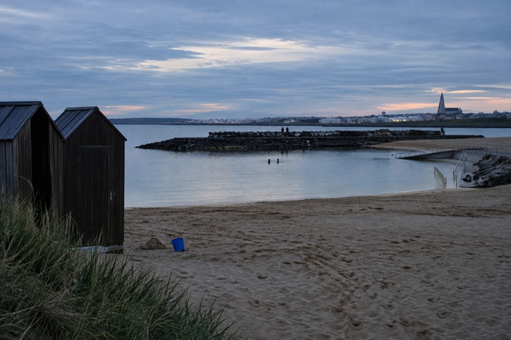 A geothermal lagoon with a sandy beach and small changing huts
