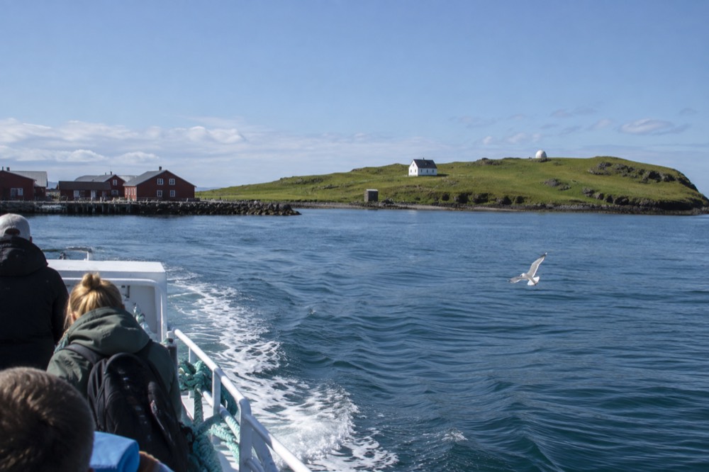 A small ferry approaching a low green island across calm water near Reykjavik on a bright day