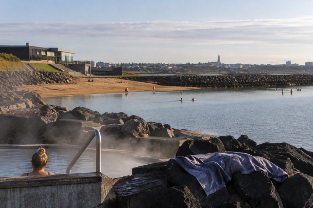 A geothermal beach area with a small sandy cove and calm water near Reykjavik under summer light