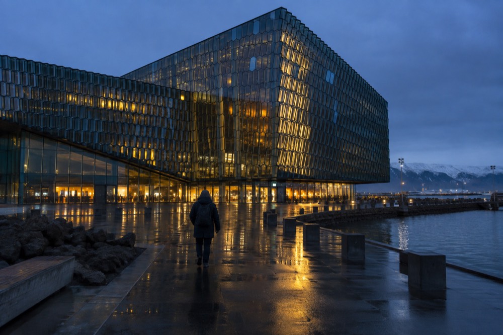 A glass concert hall glowing with light beside a dark harbour