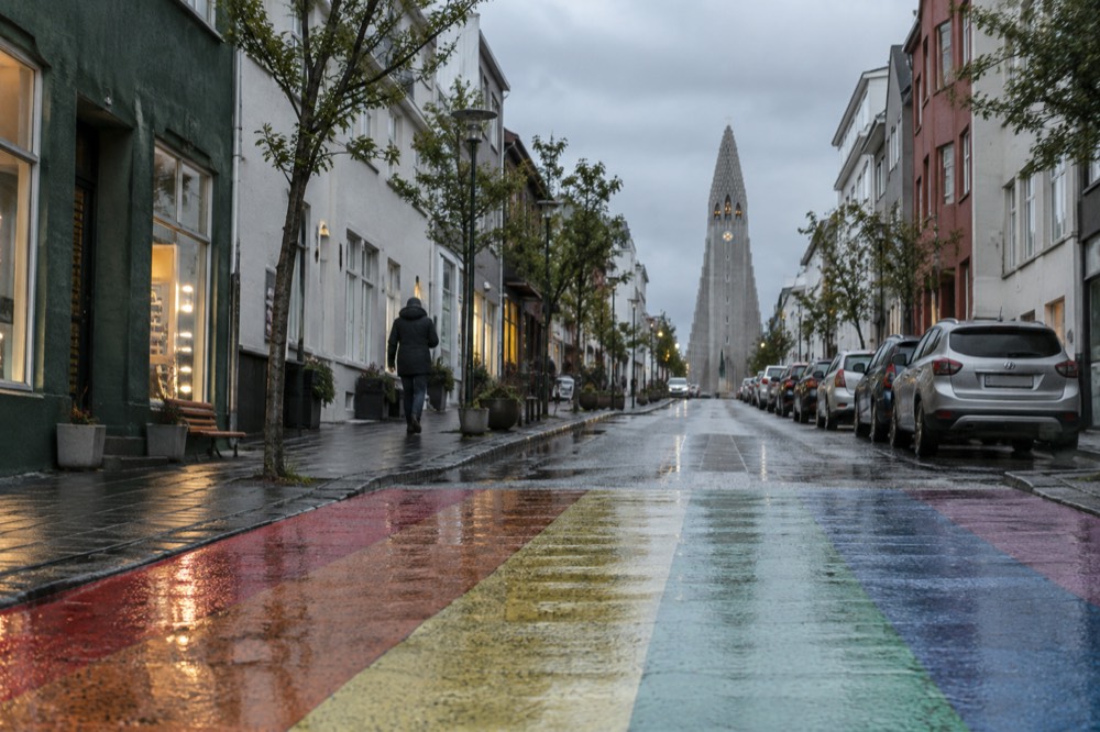 A painted rainbow crosswalk on a sloping street leading to a church