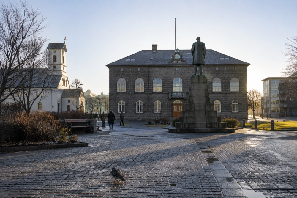 Cobblestone square in front of a stone parliament building with a statue
