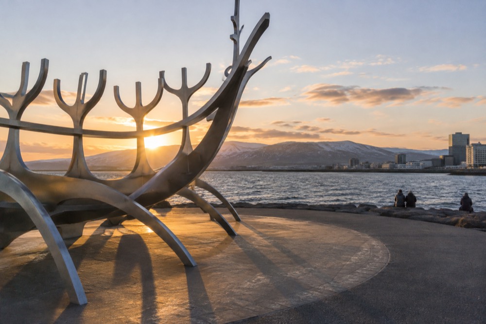 Steel boat sculpture on a waterfront promenade facing a wide bay