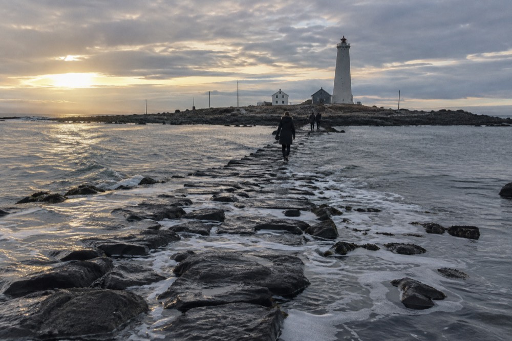 Shallow seawater washing over a low stone causeway leading to a small island with a lighthouse