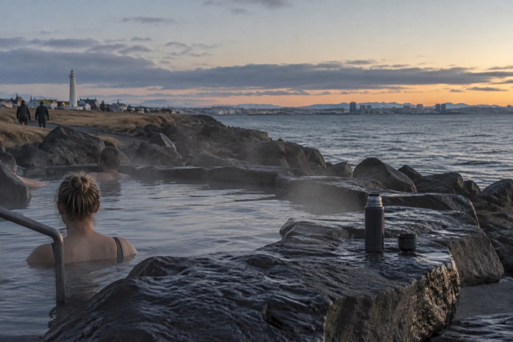 A stone foot bath beside the sea with steam rising from the water at dusk