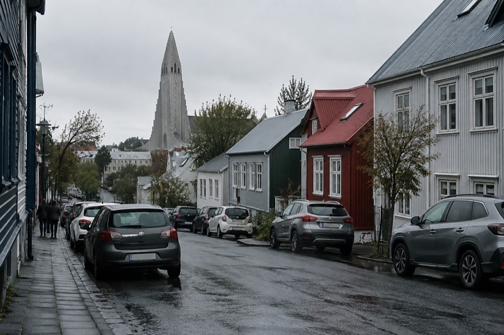 Cars parked along a sloping residential street with the Hallgrímskirkja tower above the rooftops