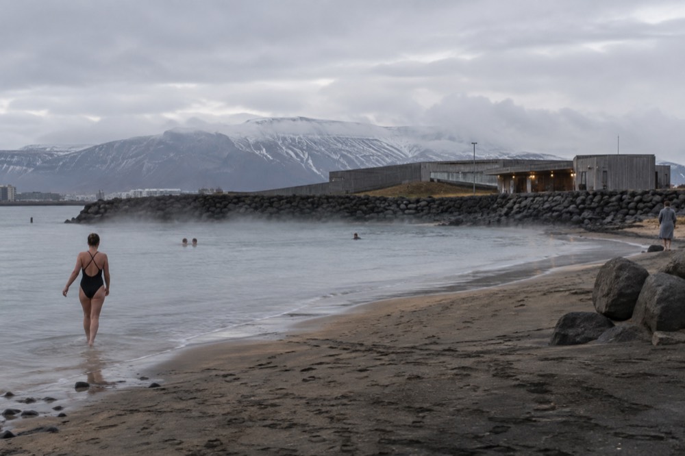 Sandy geothermal beach with steaming water at the shoreline and low hills behind