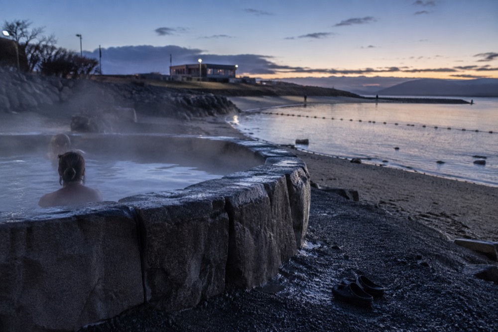 Steam rising from a stone hot pot beside a sandy beach under an overcast sky