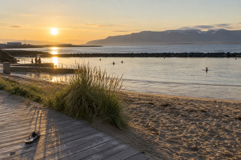 Beach at midnight with bright sky, calm lagoon water and distant mountains across the bay