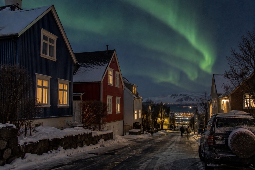 Green aurora bands above dark residential streets on the edge of Reykjavik