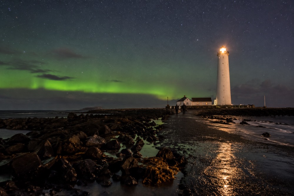Grótta lighthouse silhouette against a starry sky with green aurora on the horizon
