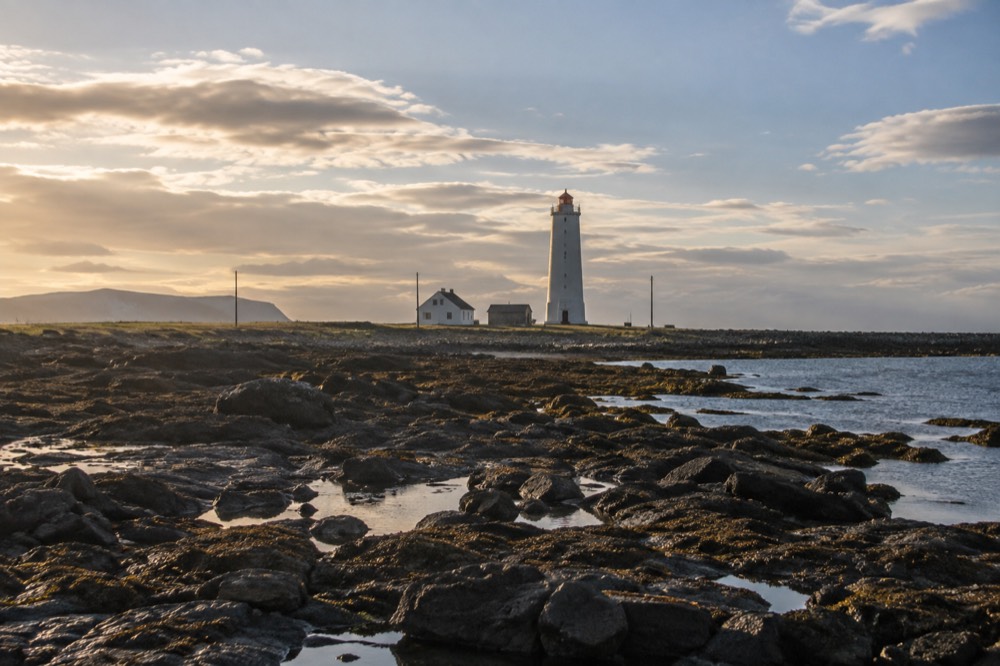 Coastal path with a lighthouse across flat tidal ground near Reykjavik