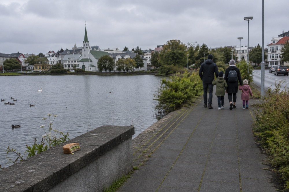 A family walking a paved path beside a pond in a city park