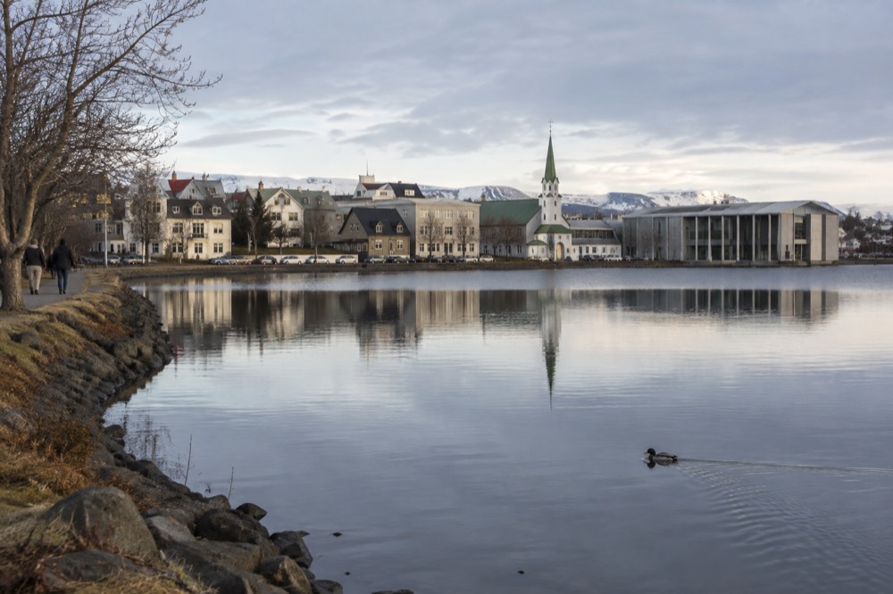 A city pond with park paths and buildings reflected in the calm water in Reykjavik