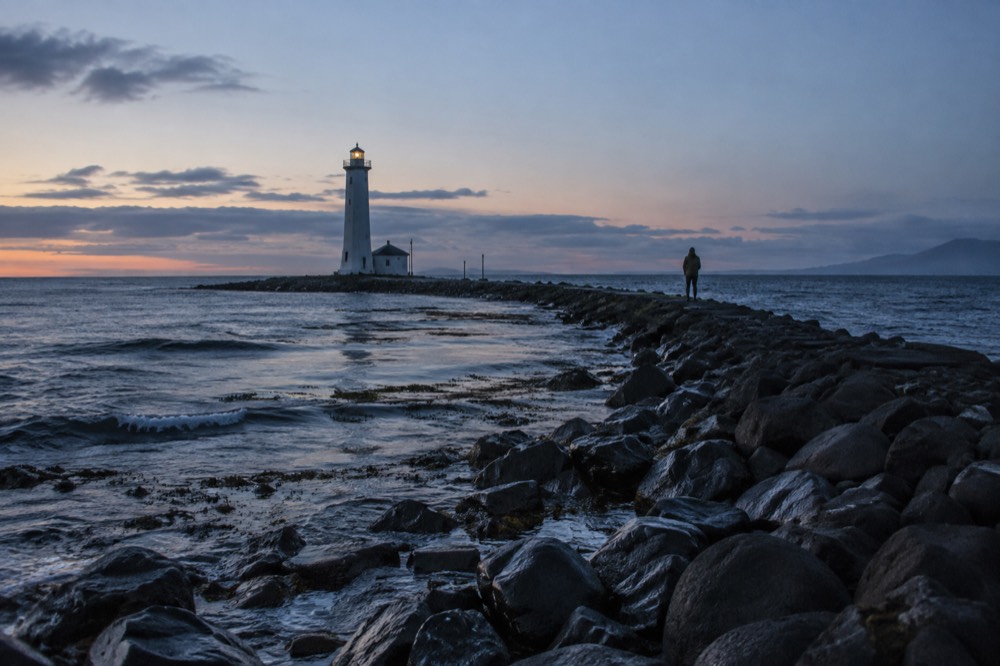 A small lighthouse on a rocky island at the end of a causeway