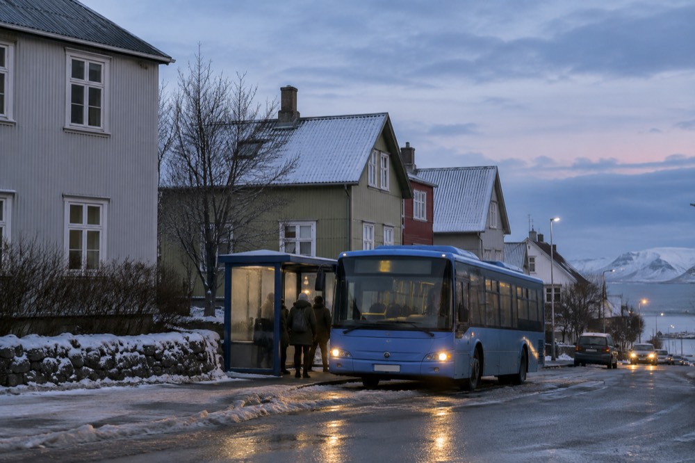 A blue city bus at a stop on a quiet street
