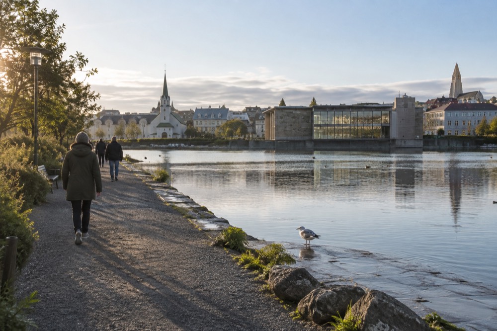 People walking the flat shoreline path of Tjörnin on a bright day with City Hall in the background