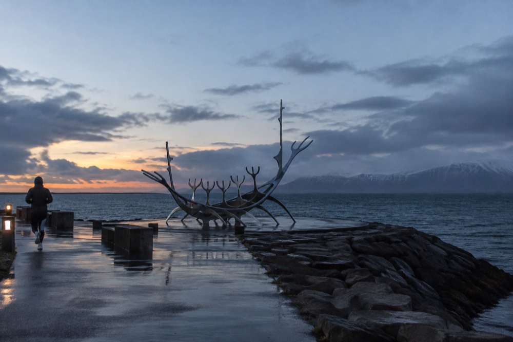 A steel sculpture of a boat shape on a waterfront path facing the bay